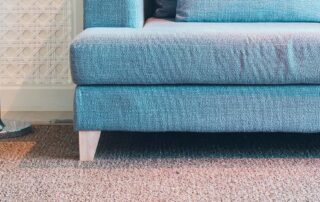 Blue couch with a lamp on a carpeted floor, highlighting 5 reasons to replace carpet flooring for a cleaner, more durable, and stylish home environment.