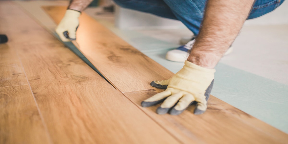 Person installing hardwood flooring with gloves.