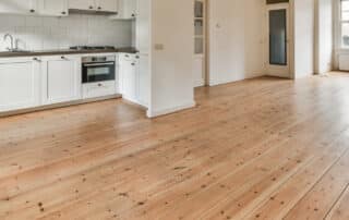 Spacious kitchen with hardwood flooring and white cabinets, answering Hardwood Flooring FAQs for earth-conscious homeowners seeking sustainable options.