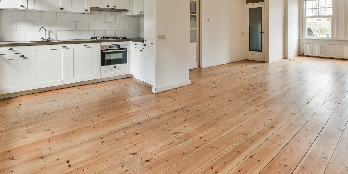 Spacious kitchen with hardwood flooring and white cabinets, answering Hardwood Flooring FAQs for earth-conscious homeowners seeking sustainable options.