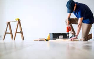 Person using drill on wooden plank indoors.