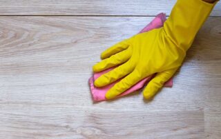 A gloved hand cleaning laminate floor with a cloth demonstrates how to clean laminate flooring effectively. Learn the best methods to maintain its shine and durability, ensuring your floors stay looking fresh and pristine over time.