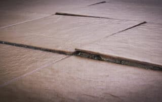 In Home Flooring highlights How to Fix Bulging Floor Tiles with lifted, cracked tiles showing damage from floor budging, poor installation, or subfloor issues.