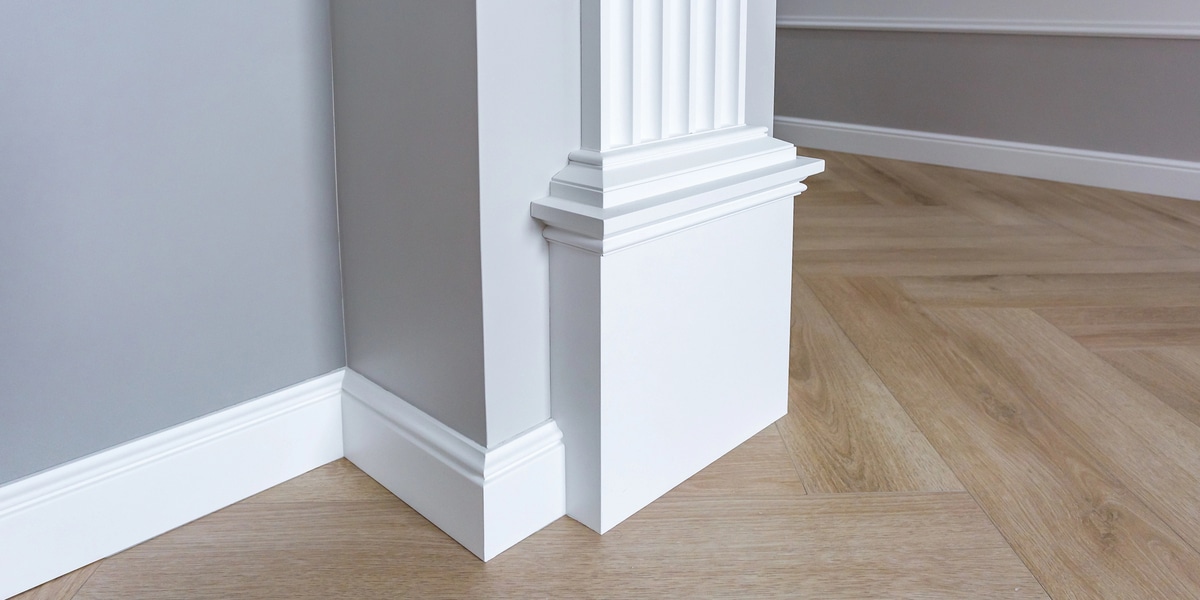 The Complete Guide to Floor Moldings & Transitions White baseboards and molding on wooden floor corners.
